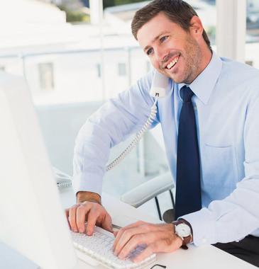 Smiling Businessman Working And Phoning At His Desk In His Office